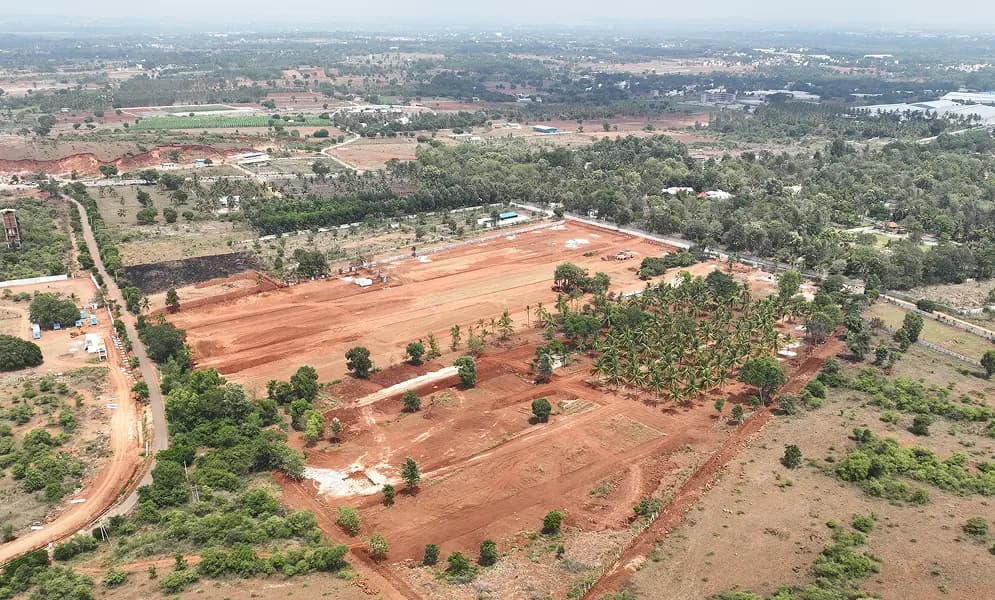 Aerial view of a cleared red-earth site surrounded by palm trees